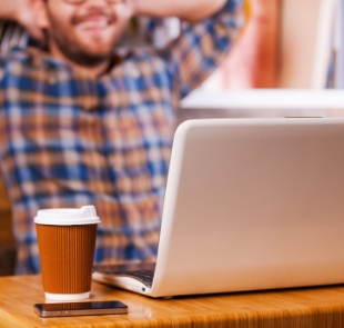 Mann an Laptop lehnt sich entspannt zurück